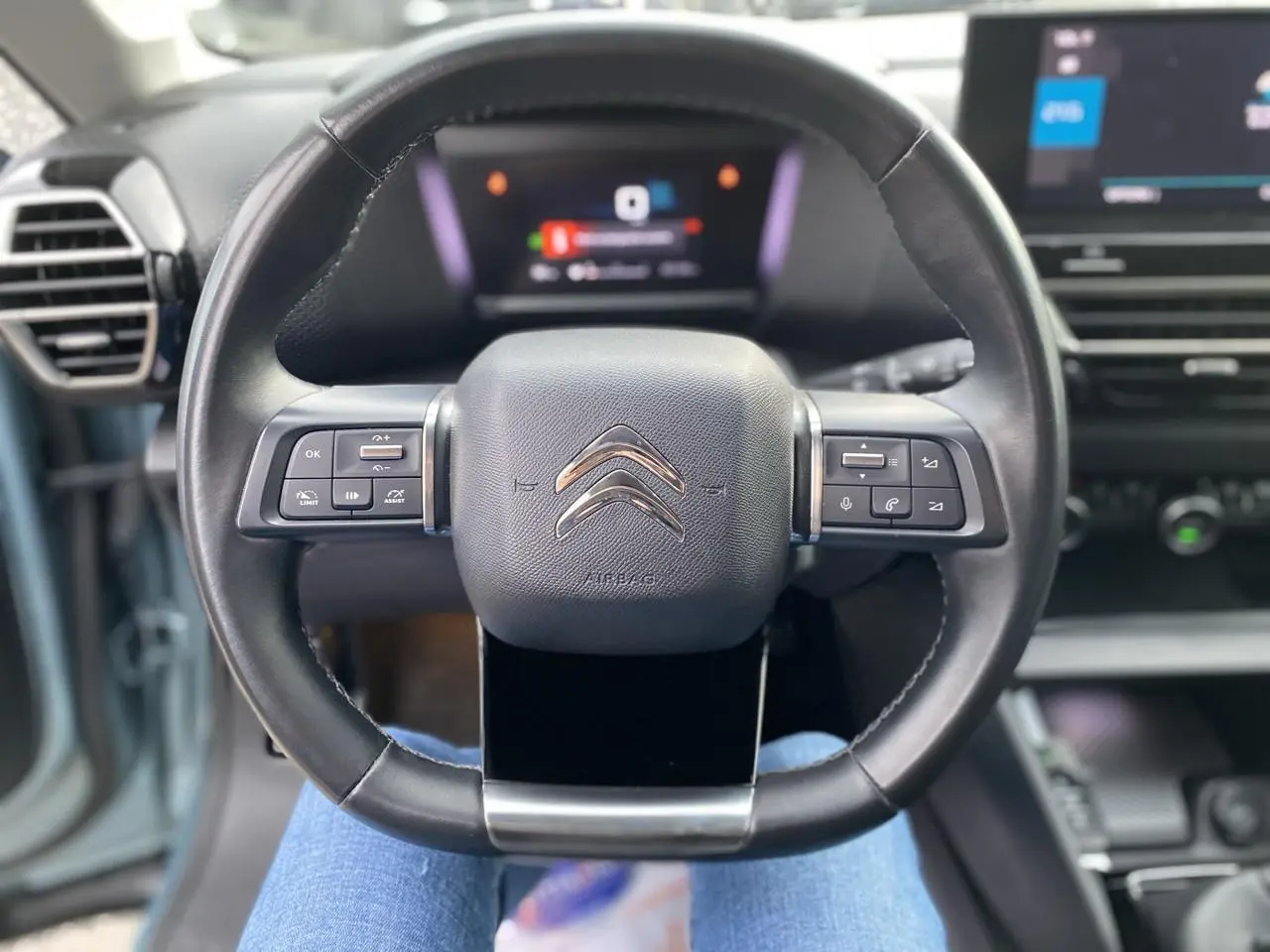 Vue rapprochée du volant cuir noir de la Citroën C4 2021 avec commandes intégrées et tableau de bord numérique flou.