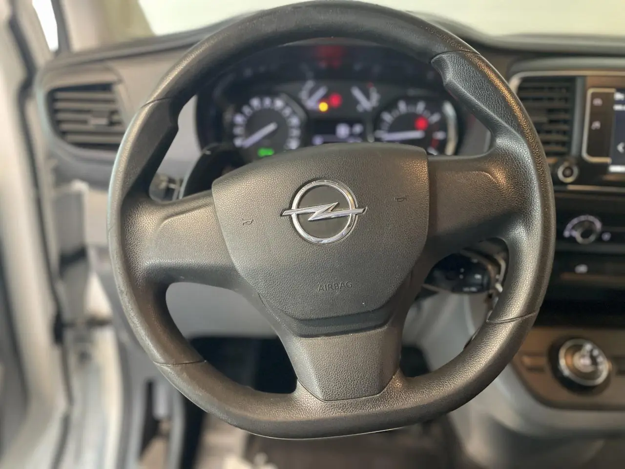 Volant noir avec logo Opel en gros plan, tableau de bord et partie de la planche de bord du Vivaro blanc visible en arrière-plan.
