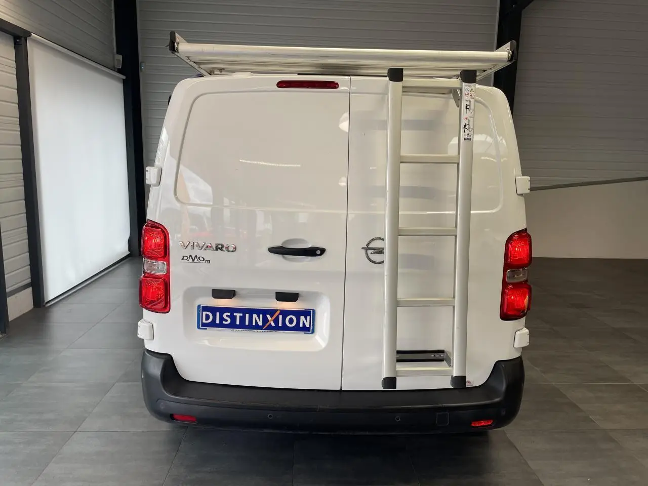 Vue arrière d'un fourgon blanc Opel Vivaro 2021 avec échelle fixée sur la porte droite et bouclier noir.
