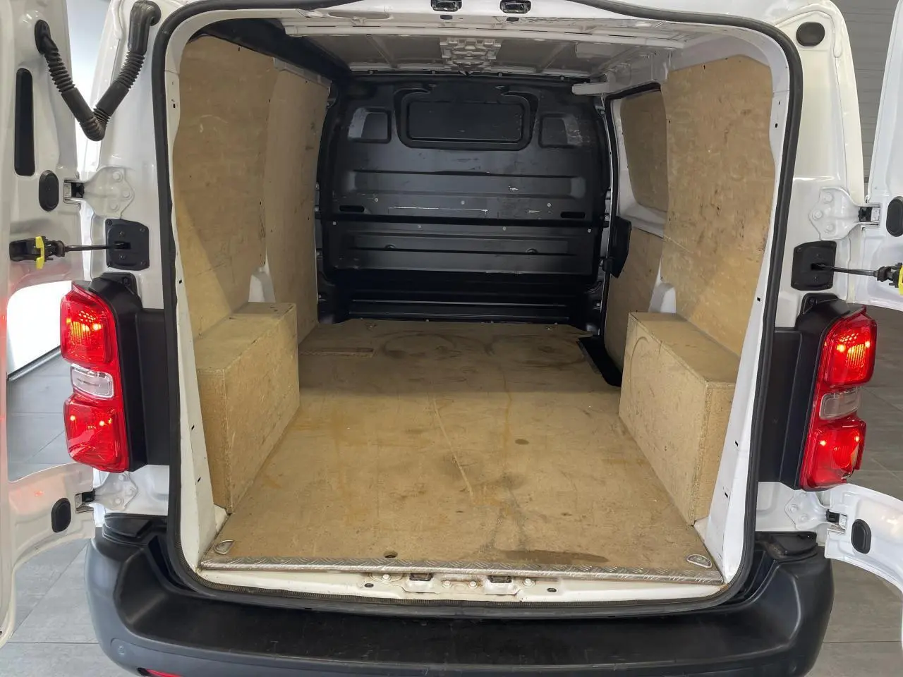 Vue arrière ouverte du fourgon Opel Vivaro blanc montrant l'espace de chargement avec cloison tôlée noire et plancher protégé.
