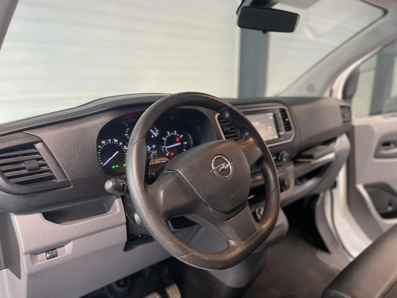 Vue intérieure côté conducteur de l'Opel Vivaro blanc 2021, volant noir avec logo Opel et tableau de bord moderne.
