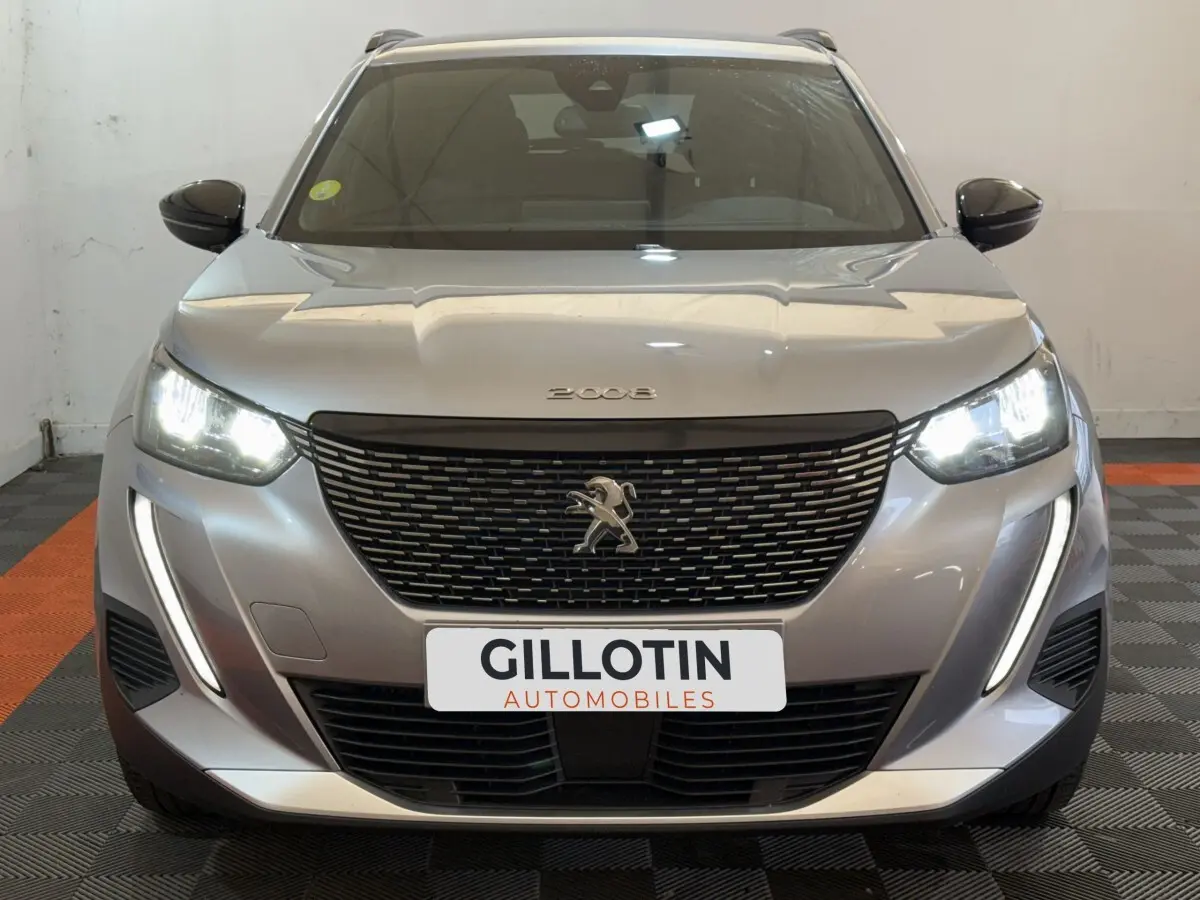 Vue avant d'une Peugeot 2008 gris clair avec phares LED allumés et calandre noire distinctive.
