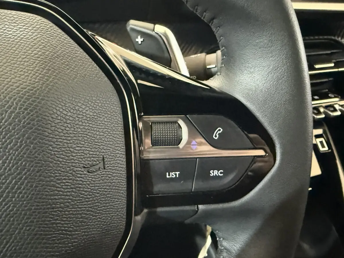Gros plan sur les commandes gauche du volant en cuir noir du Peugeot 2008 gris clair, avec boutons multifonctions visibles.