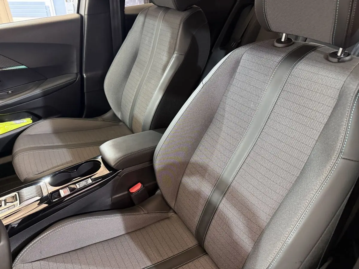 Vue rapprochée des sièges avant gris clair et tissu avec surpiqûres, console centrale noire brillante d’une Peugeot 2008 2023.