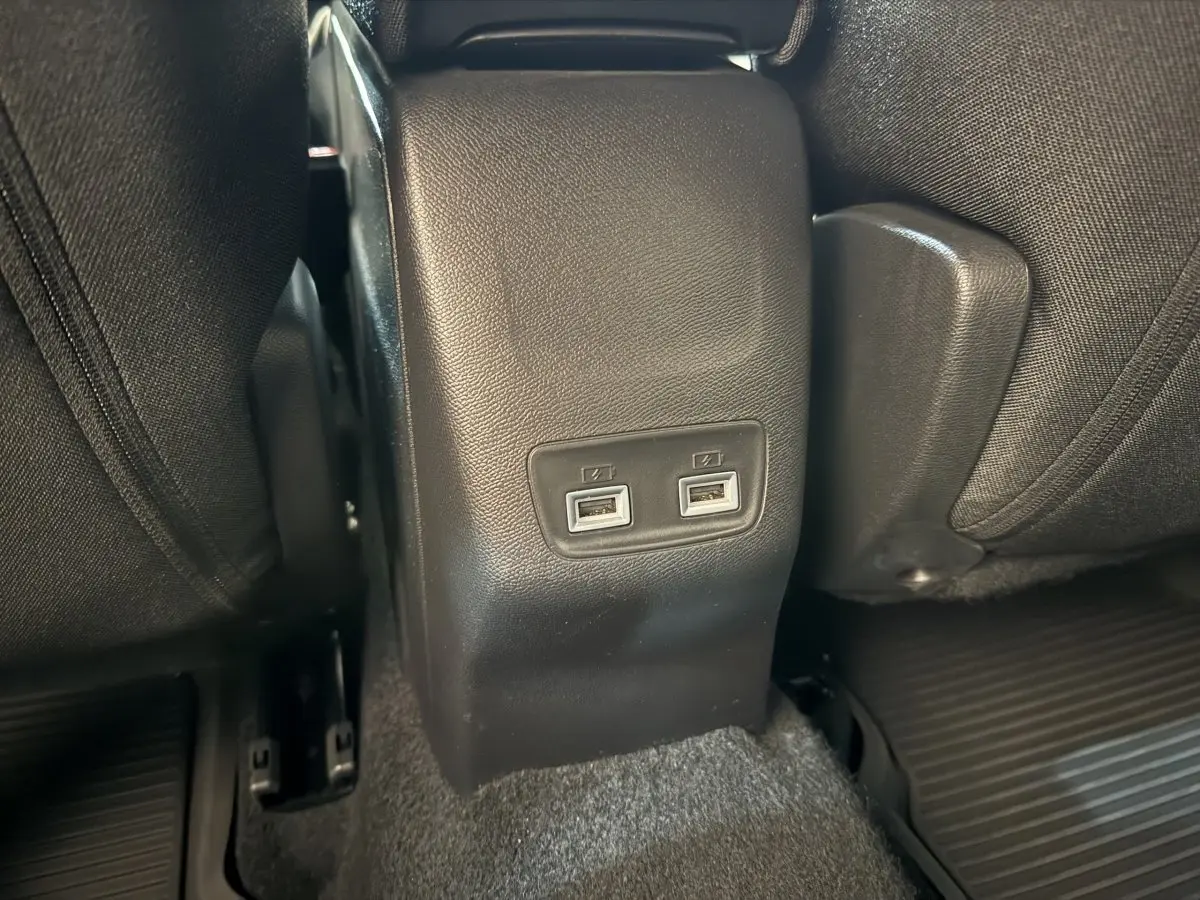 Prise double USB arrière entre les sièges noirs d’un Peugeot 2008 gris clair, vue rapprochée du plancher.
