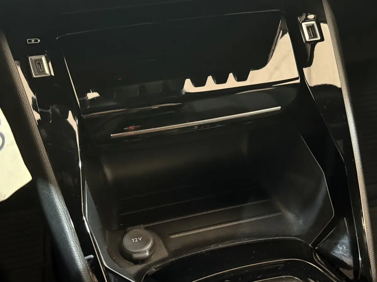Gros plan sur la console centrale noire brillante du Peugeot 2008 2023 avec prise 12V visible.