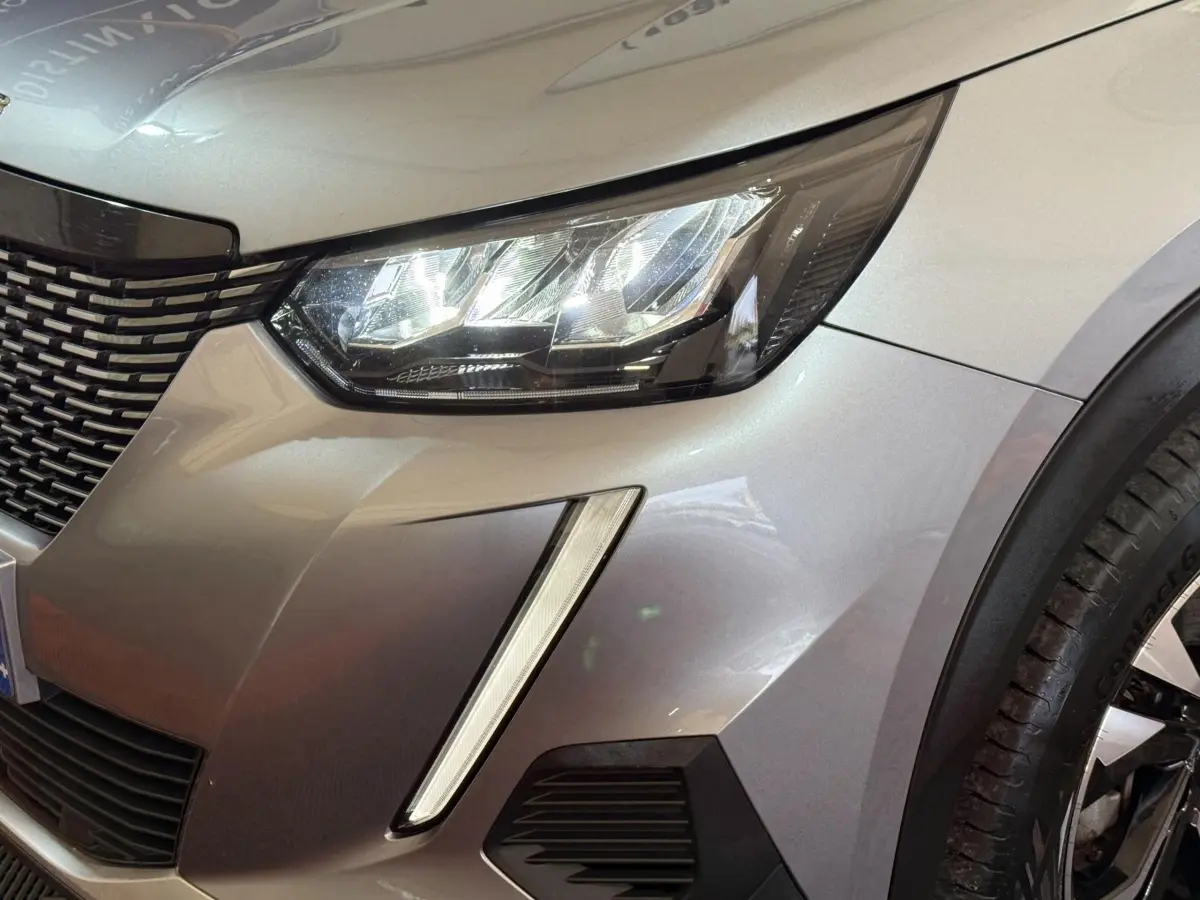 Gros plan sur l'avant droit gris clair du Peugeot 2008 2023, mettant en valeur le phare LED et la calandre distinctive.