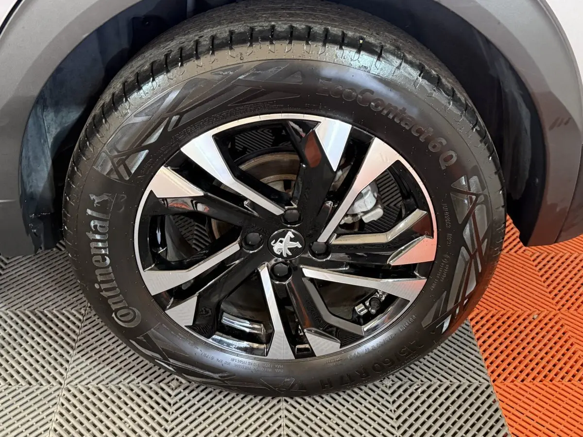 Gros plan sur la roue avant droite du Peugeot 2008 gris clair, jante alliage noire et argentée au design moderne.