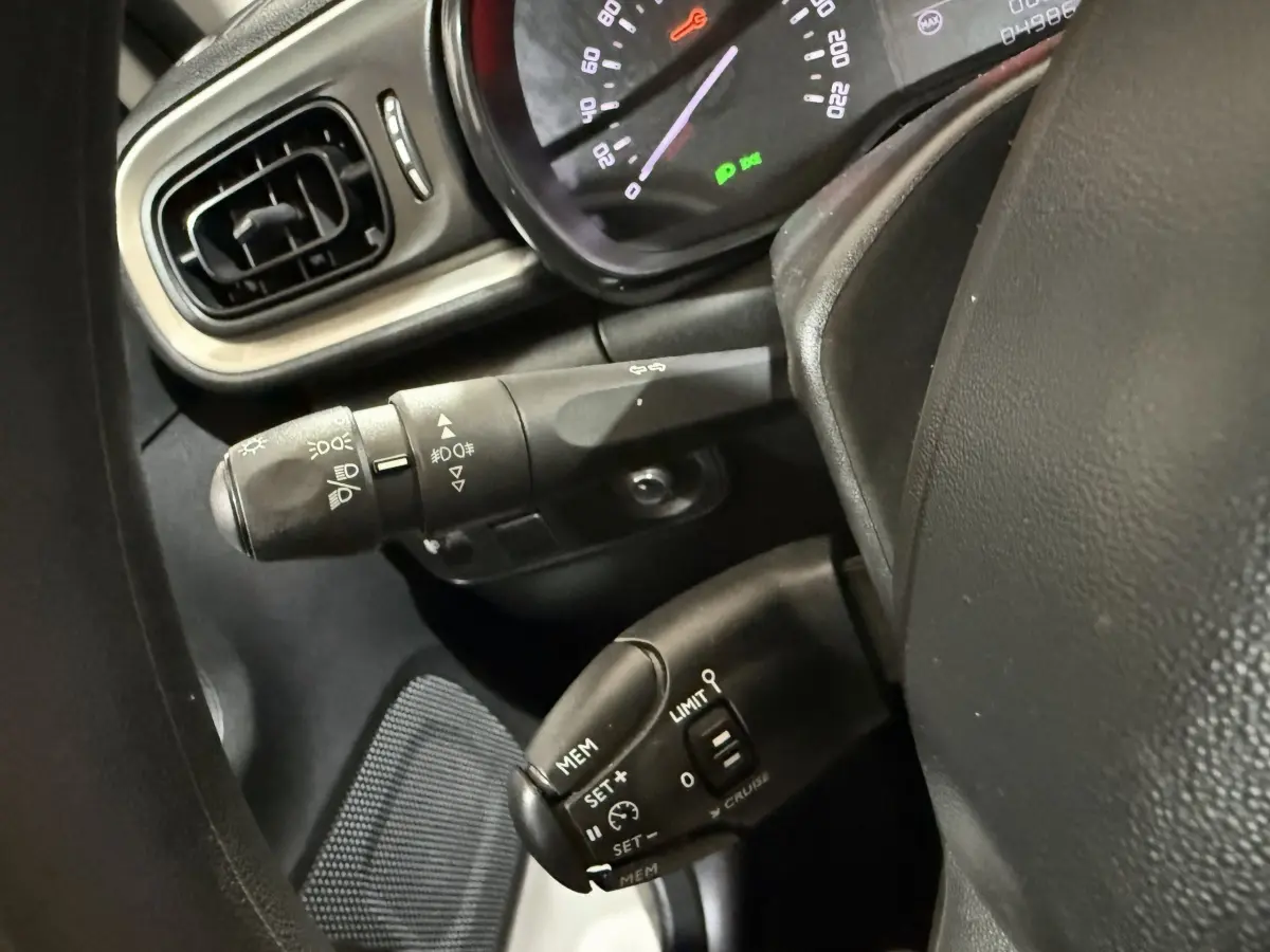 Gros plan sur la colonne de direction et commandes au volant d'une Citroën C3 blanche, tableau de bord partiellement visible.