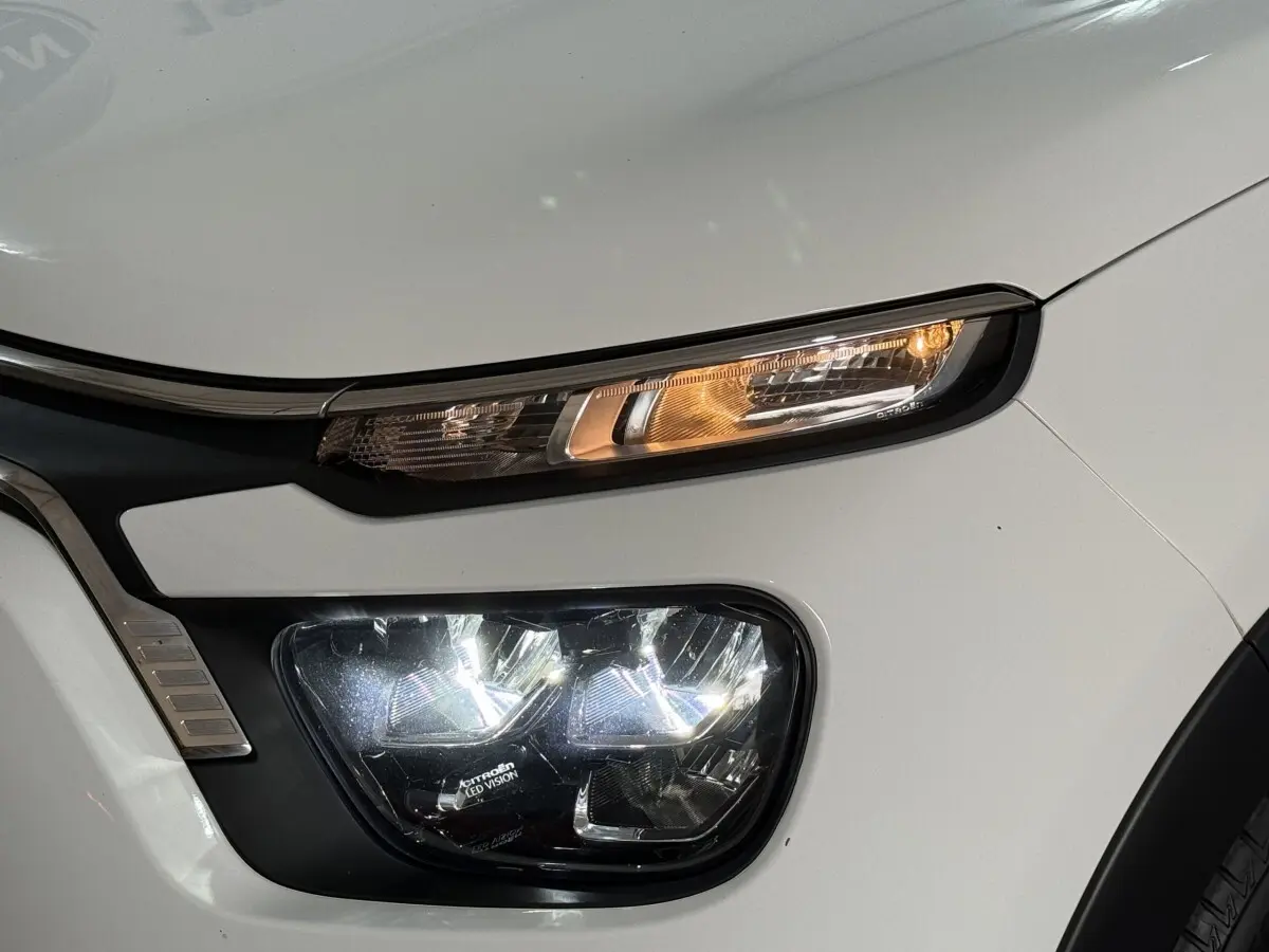 Gros plan sur le phare avant droit blanc d'une Citroën C3 2021 avec éclairage LED et clignotant allumé.