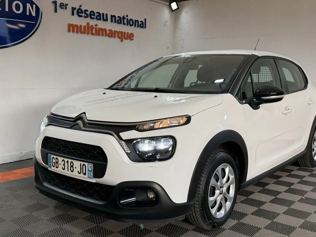 Vue 3/4 avant droite d'une Citroën C3 blanche 2021 avec phares allumés et détails noirs contrastants.