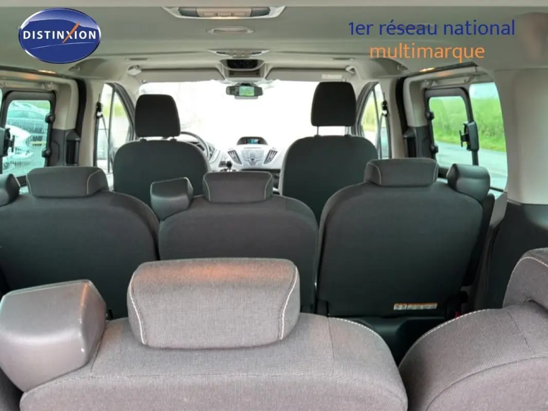 Vue intérieure arrière du Ford Tourneo Custom gris foncé, montrant les sièges passagers et le tableau de bord à l'avant.