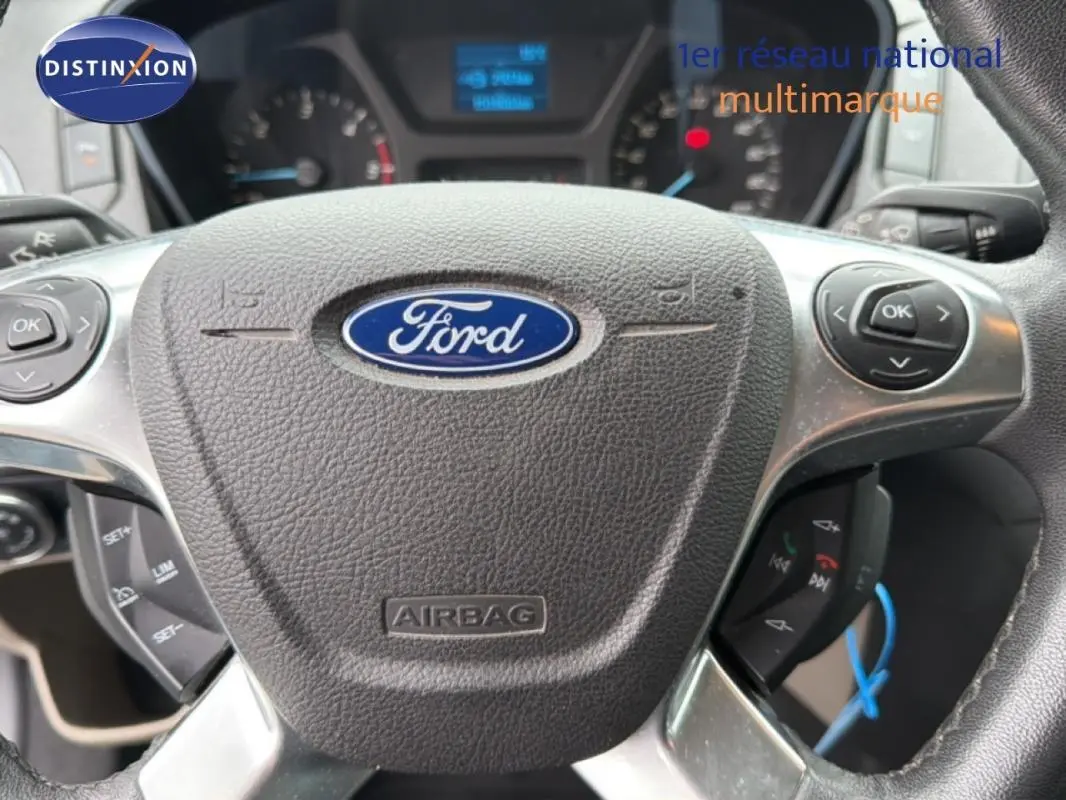 Gros plan sur le volant Ford gris foncé du Tourneo Custom 2015 avec commandes intégrées et tableau de bord flou en arrière-plan.