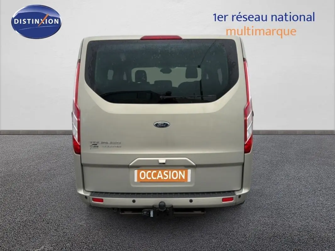 Vue arrière d’un Ford Tourneo Custom gris foncé avec attelage et vitres surteintées, en stationnement sur sol goudronné.