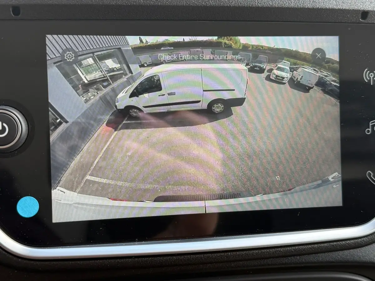 Vue caméra arrière montrant un utilitaire blanc Iveco Daily 35S18 garé côté gauche près d’un bâtiment.