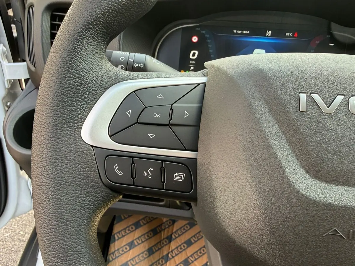 Gros plan sur le volant gris foncé de l'Iveco Daily 2026, avec commandes multifonctions et tableau de bord numérique en arrière-plan.