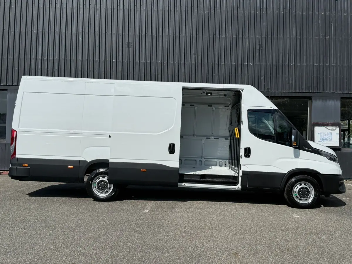 Fourgon Iveco Daily blanc vu de profil droit avec porte latérale coulissante ouverte montrant l’espace de chargement vide.