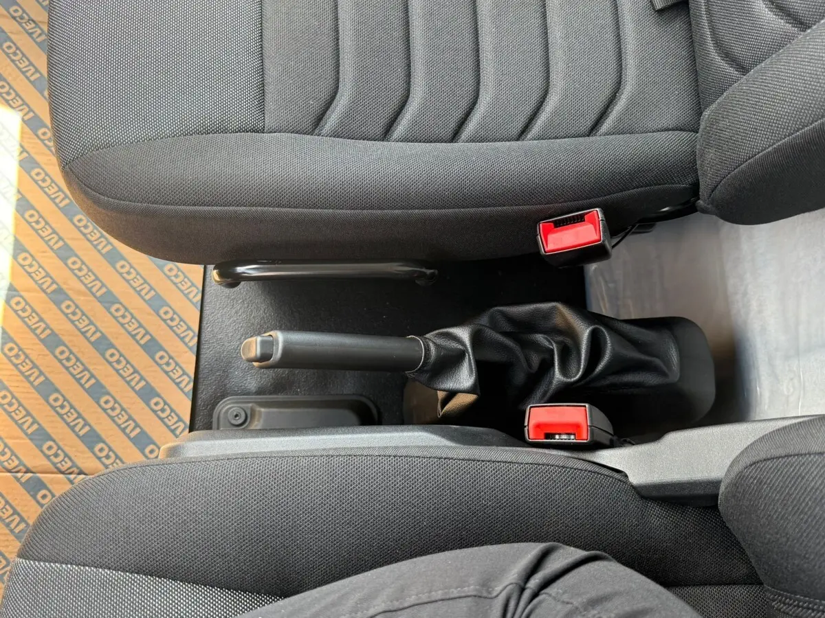 Vue plongeante sur la console centrale et les sièges noirs du fourgon Iveco Daily blanc, avec frein à main visible.
