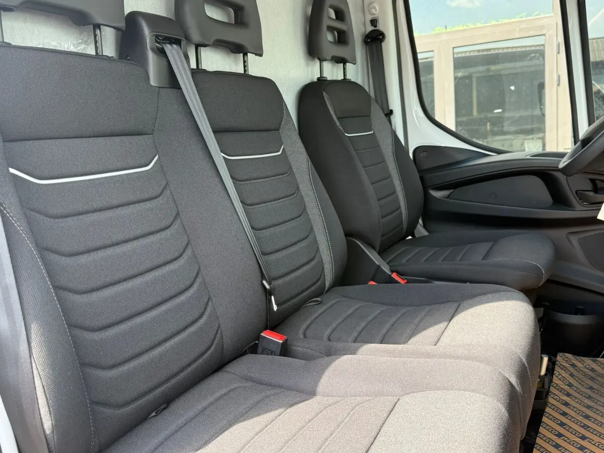 Vue intérieure côté droit montrant les sièges avant noirs du fourgon Iveco Daily blanc, avec ceinture de sécurité centrale visible.