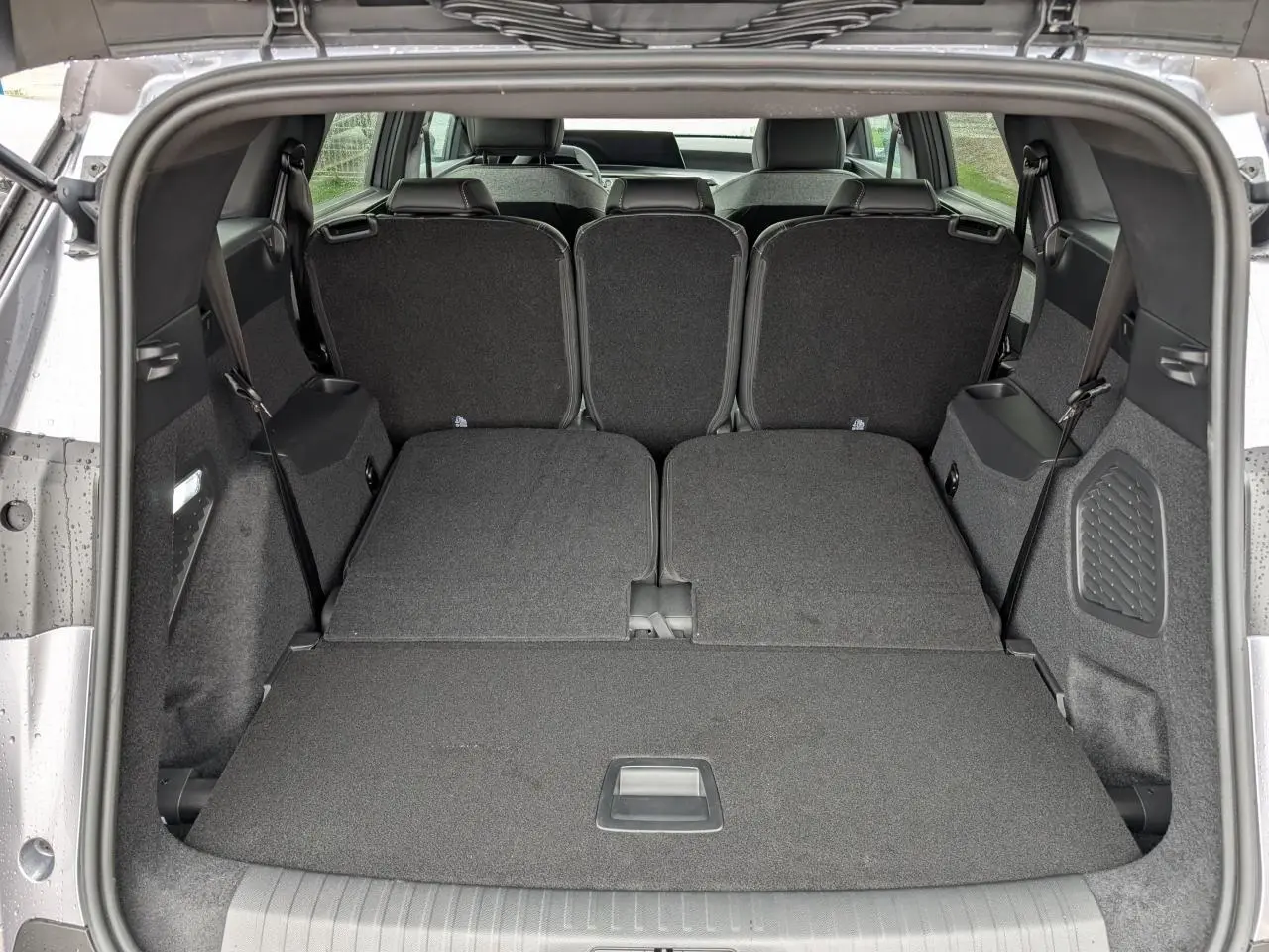 Coffre ouvert du Peugeot 5008 gris Artense avec banquette arrière rabattue, offrant un espace de chargement plat.