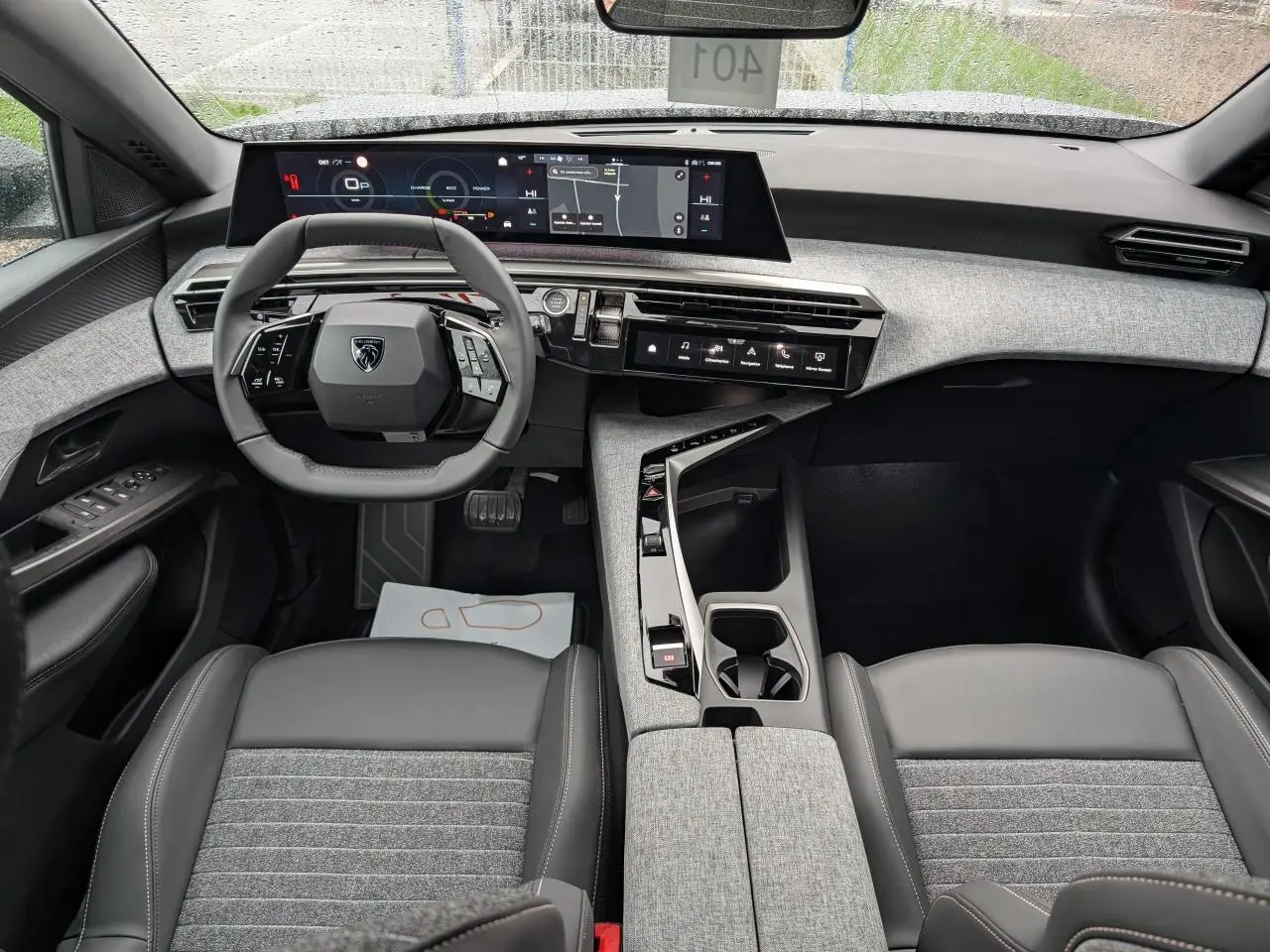 Intérieur du Peugeot 5008 2025 vu de face, avec tableau de bord gris clair et sièges tissu gris foncé.