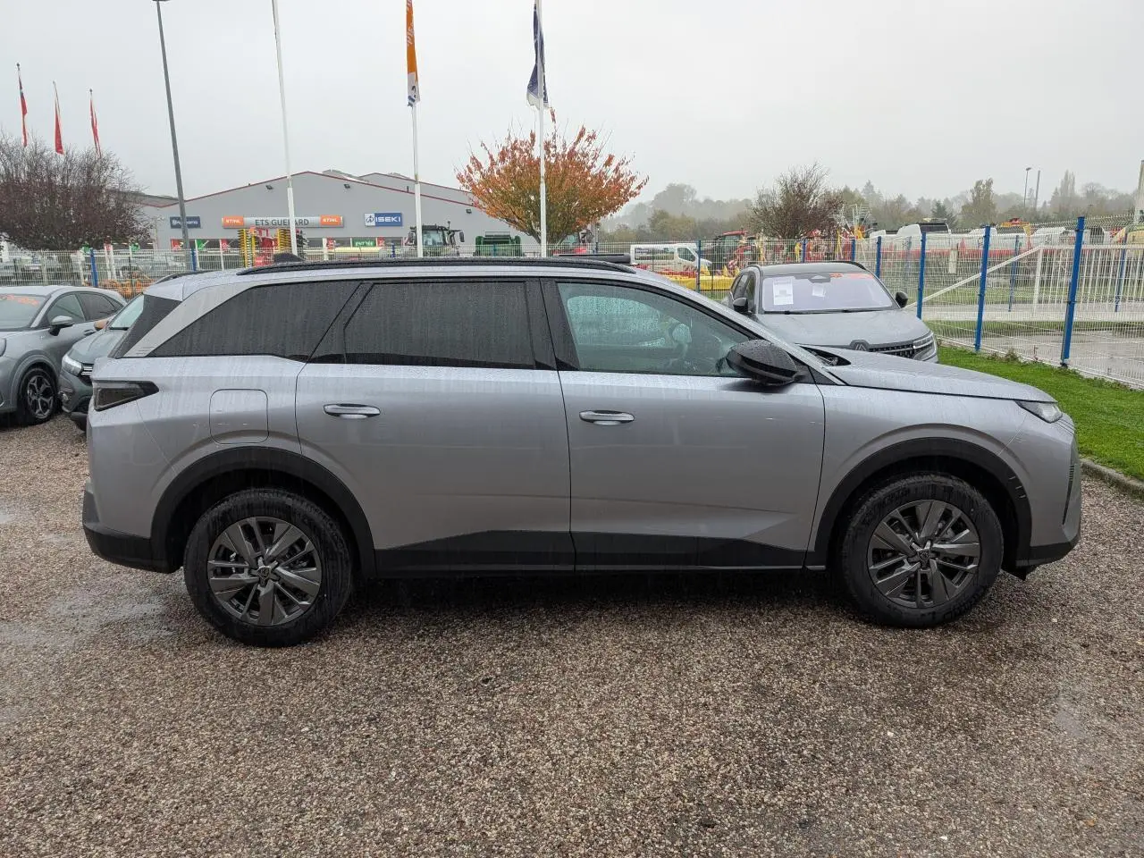 Profil côté gauche du Peugeot 5008 gris Artense 2025 avec jantes alliage et vitres teintées sur parking.