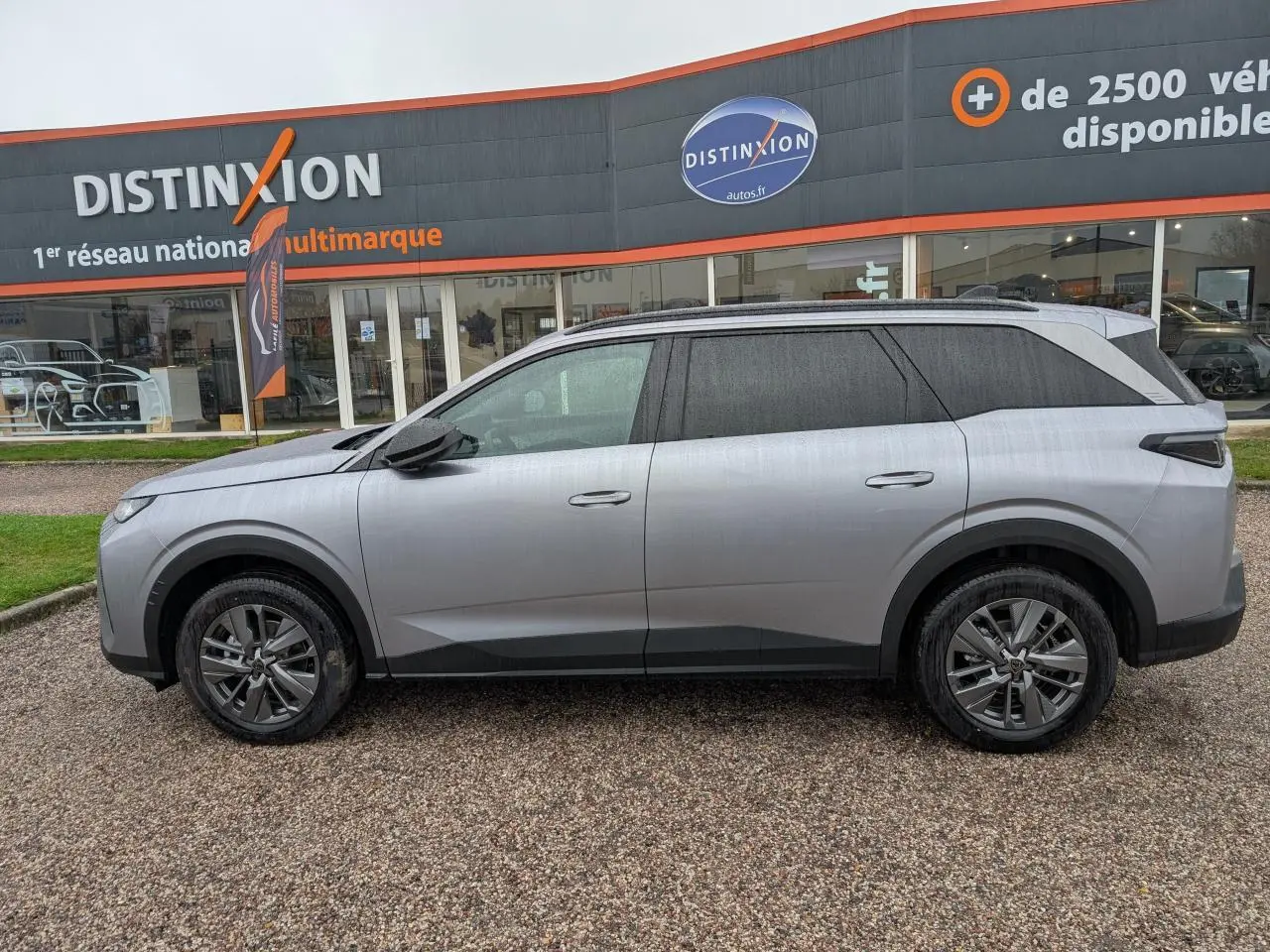 Peugeot 5008 gris Artense vue de profil côté gauche, stationnée devant un concessionnaire Distinxion