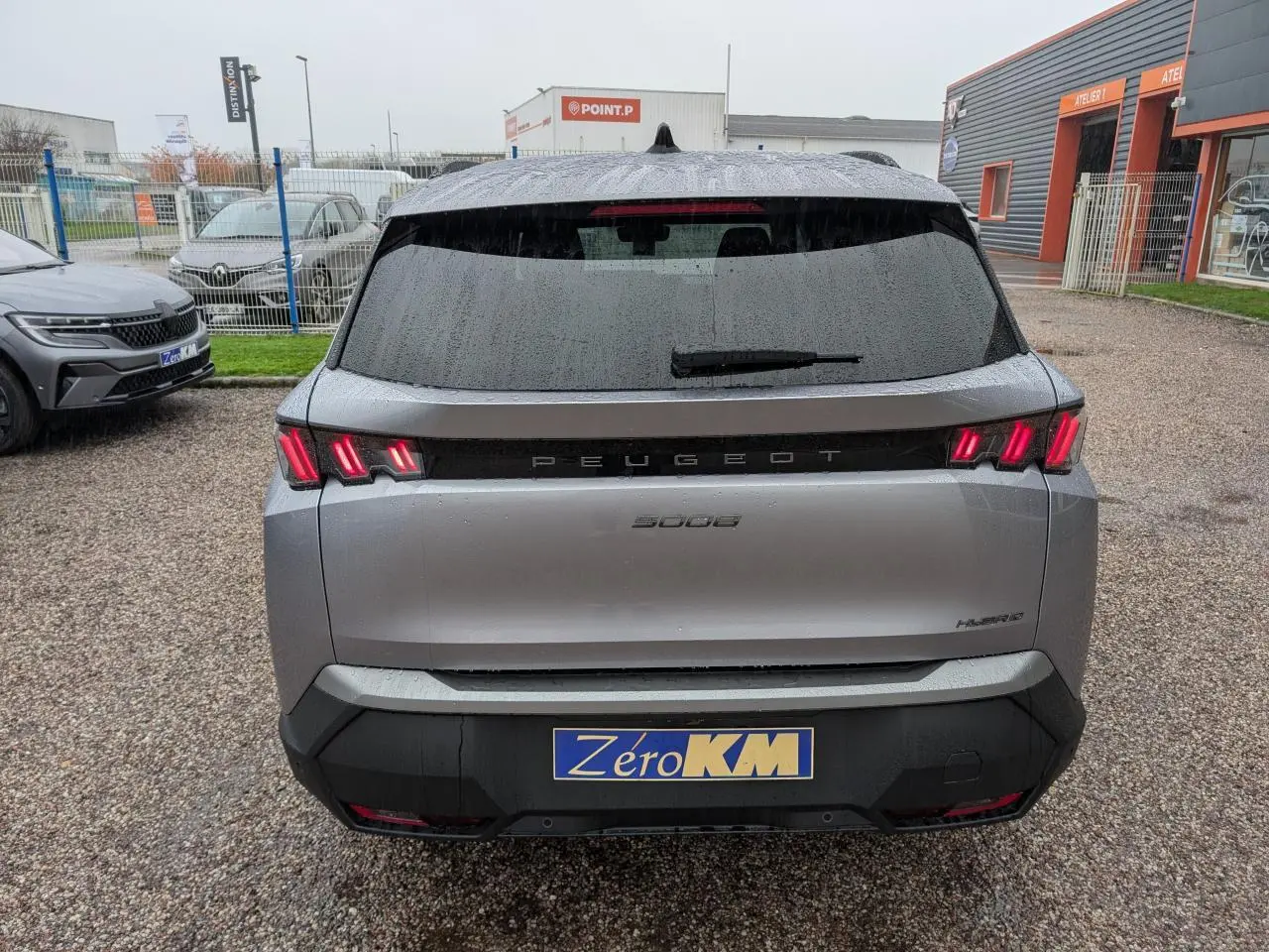 Vue arrière sous la pluie d’un Peugeot 5008 gris Artense avec feux arrière à trois griffes LED et bandeau noir laqué.