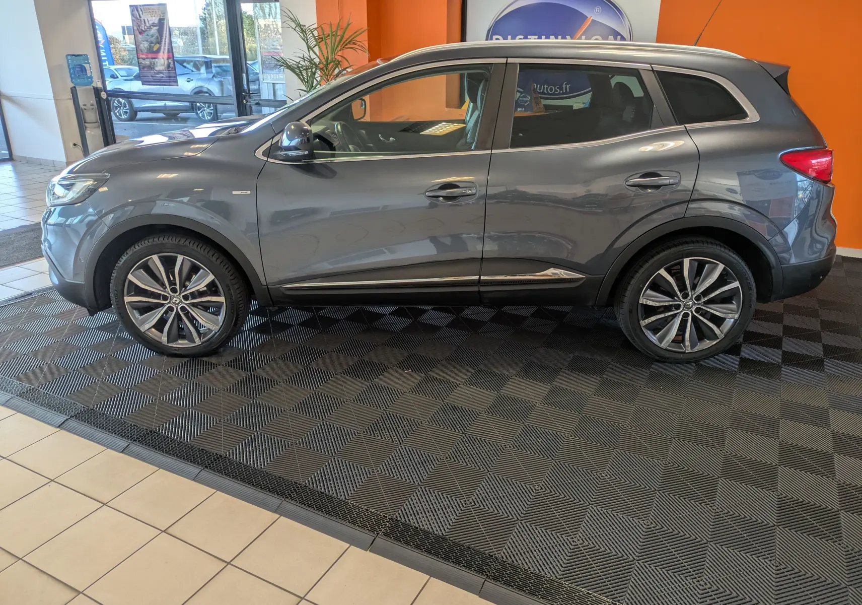 Profil côté gauche d'un Renault Kadjar gris 2017 exposé en intérieur, avec jantes bi-ton et toit ouvrant visible.