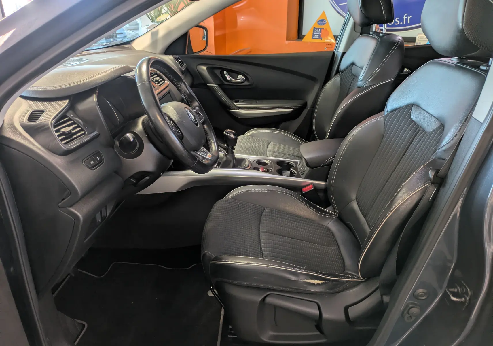 Intérieur avant droit du Renault Kadjar gris 2017, sièges en cuir noir et tableau de bord avec volant multifonction.