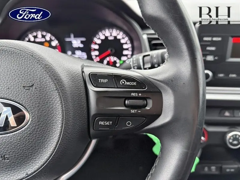 Gros plan sur le volant cuir noir d’une KIA Rio 2018, avec commandes de régulateur de vitesse visibles à droite.