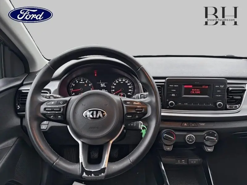 Vue intérieure centrée sur le volant cuir noir d'une KIA Rio 2018, avec tableau de bord et console centrale visibles.