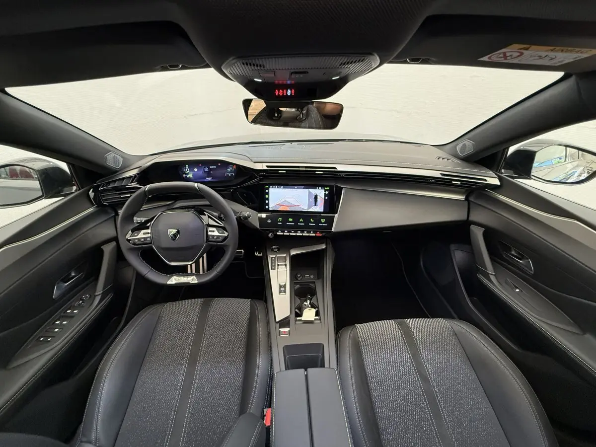 Vue intérieure avant du Peugeot 308 Hybrid 136 e-DCS6 GT 2024, avec tableau de bord numérique et sièges gris foncé.