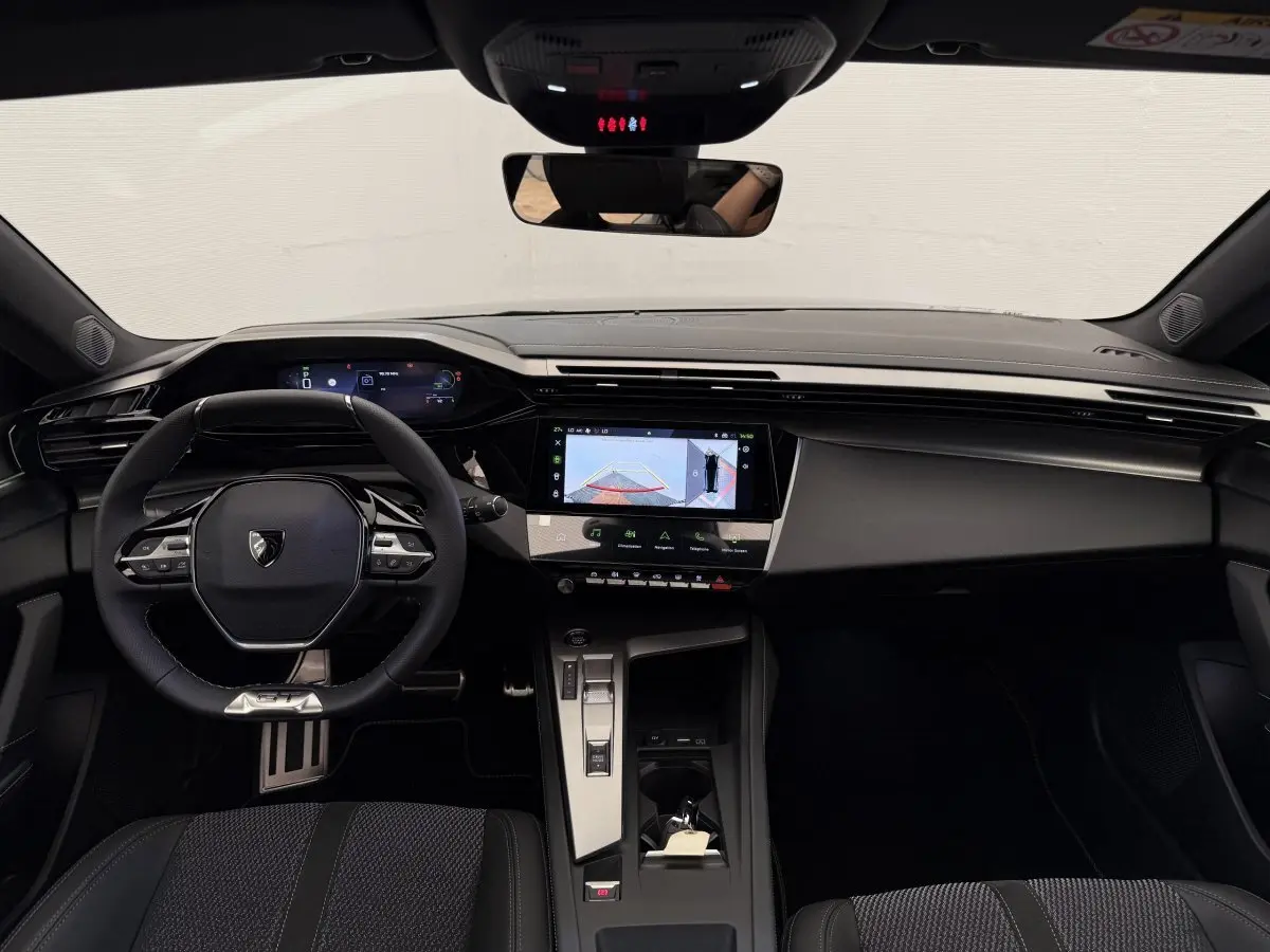 Vue intérieure frontale du tableau de bord noir du Peugeot 308 Hybrid 136 e-DCS6 GT avec écran tactile central et volant multifonctions.