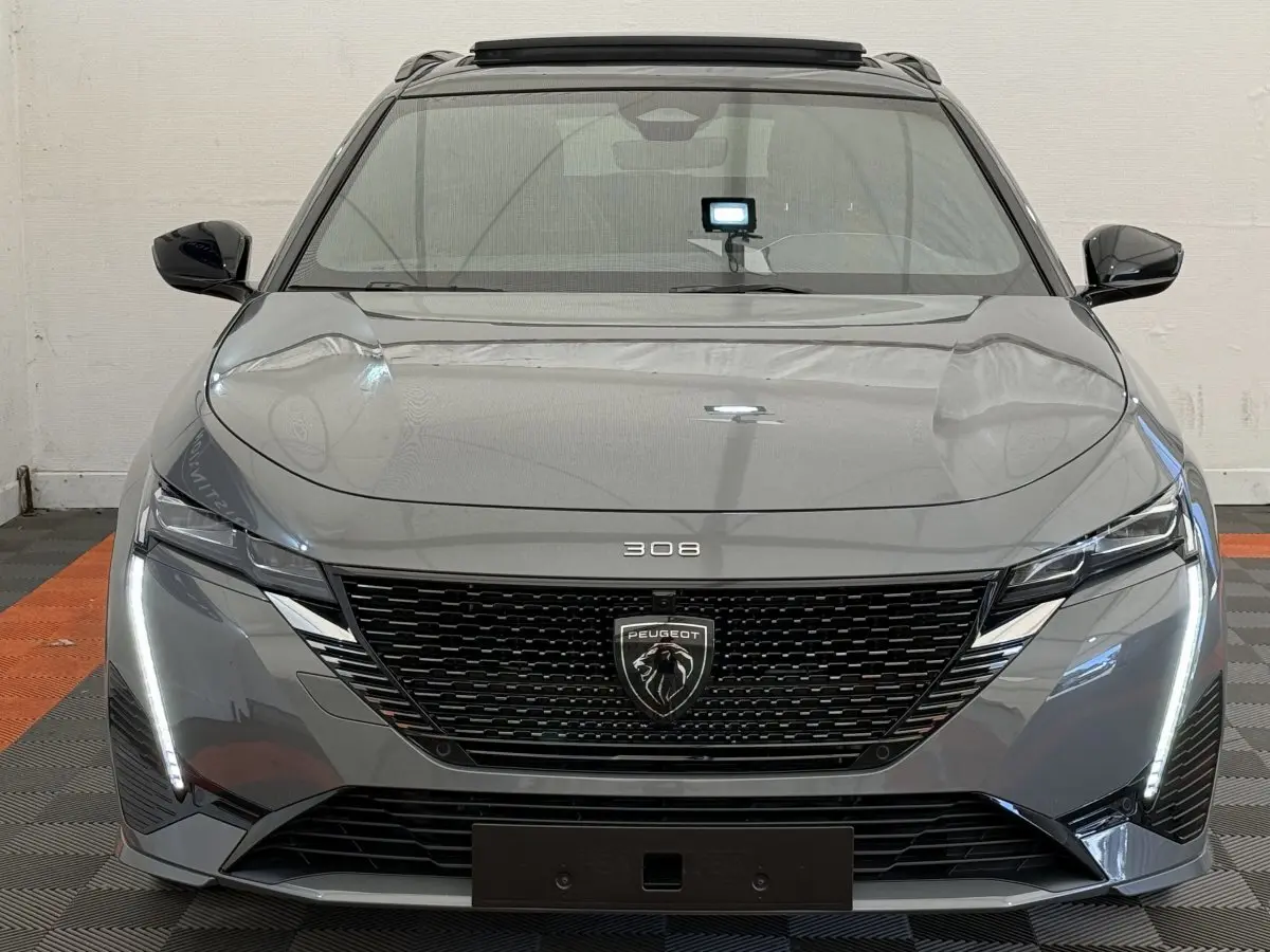 Vue frontale d'une Peugeot 308 Hybrid gris foncé avec calandre noire et feux LED verticaux allumés.