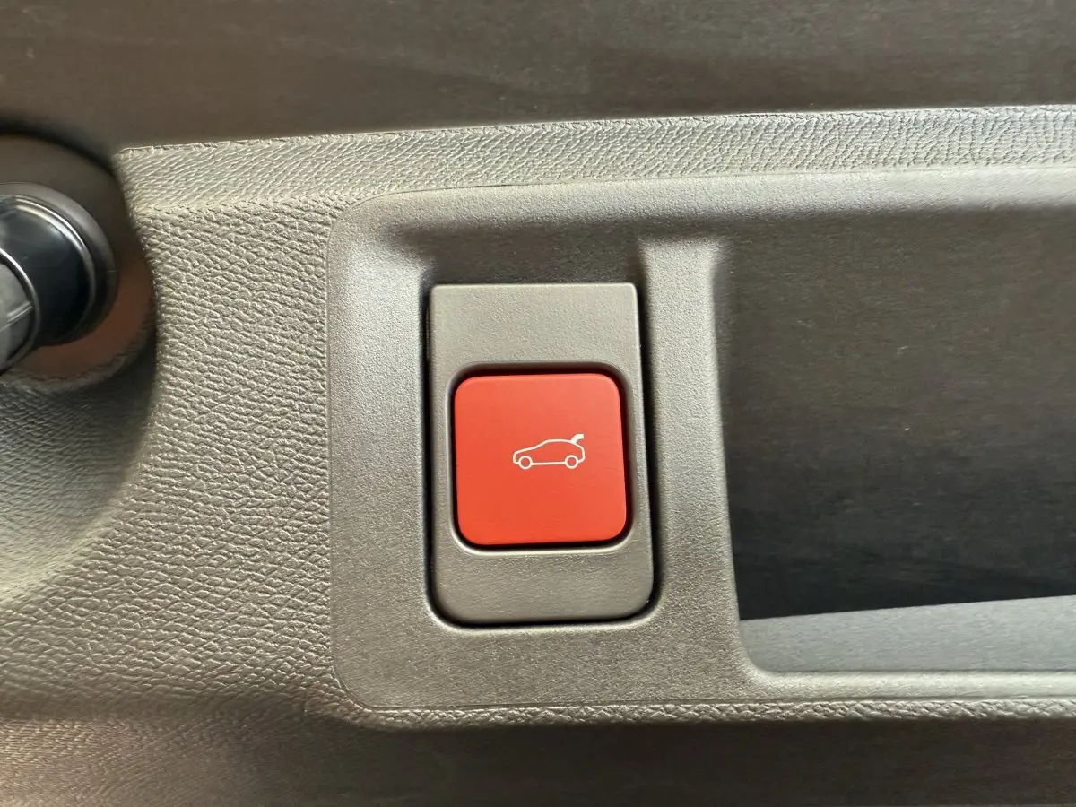 Bouton rouge d'ouverture du coffre sur la garniture intérieure grise d'une Peugeot 308 Hybrid 136 e-DCS6 GT.
