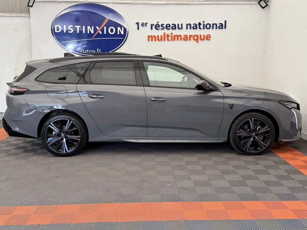 Profil droit d'une Peugeot 308 Hybrid 136 e-DCS6 GT gris foncé, avec jantes noires et toit panoramique visible.