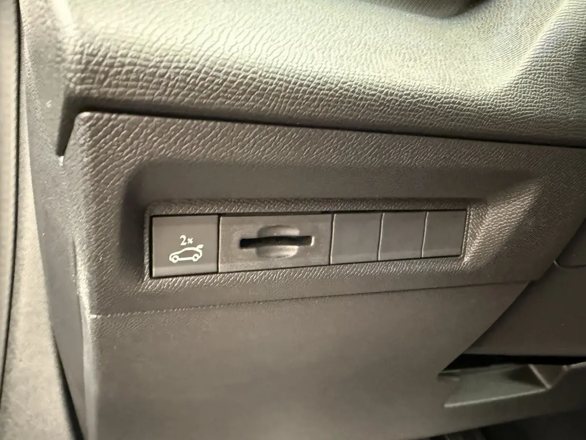 Gros plan sur le bouton d'ouverture du coffre dans l'habitacle d'une Peugeot 308 Hybrid gris foncé.