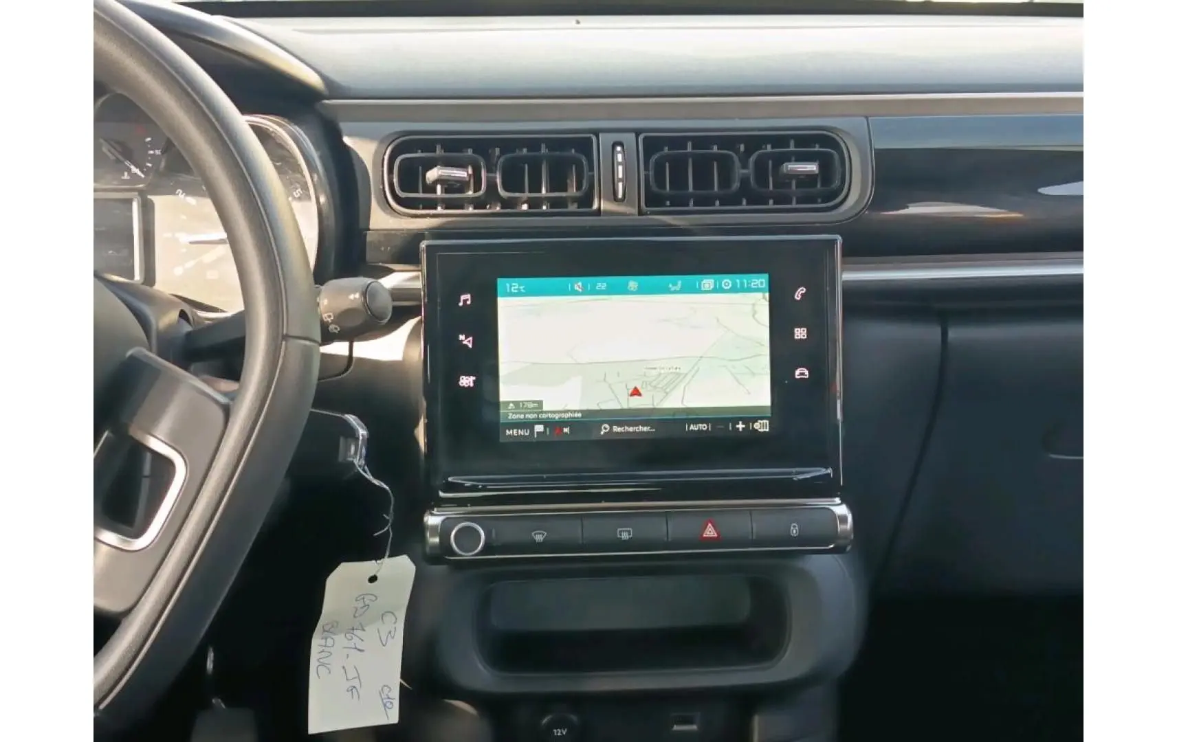 Vue intérieure centrée sur la console centrale noire avec écran GPS tactile et volant partiel d'une Citroën C3 blanche.