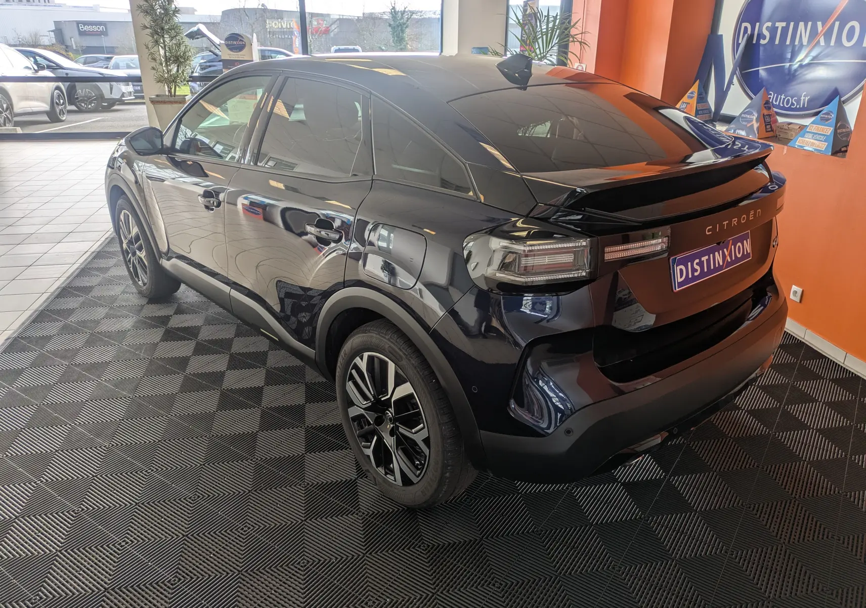 Vue 3/4 arrière droite d'une Citroën C4 hybride 2025 bleu éclipse avec jantes alliage et toit noir en showroom.