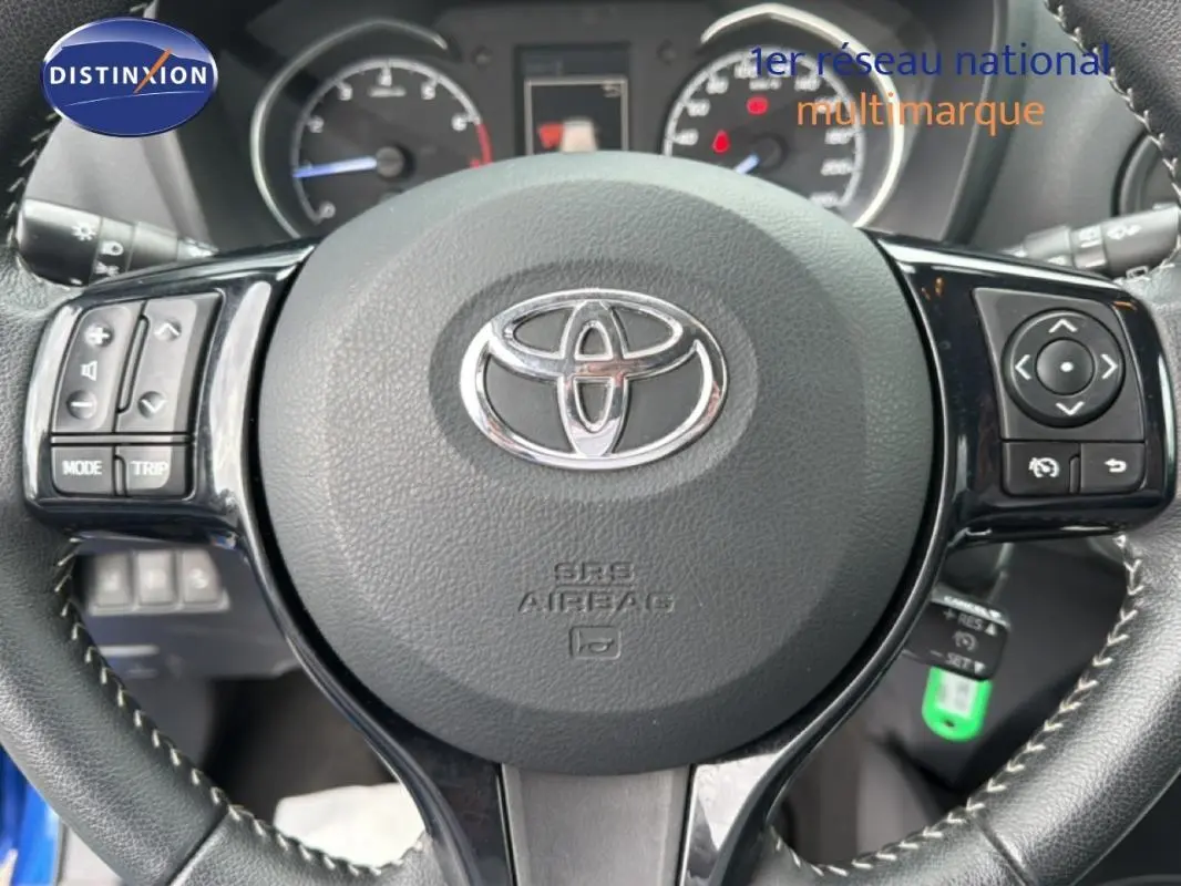 Gros plan sur le volant multifonctions en cuir noir de la Toyota Yaris bleu foncé, avec commandes intégrées et logo central.