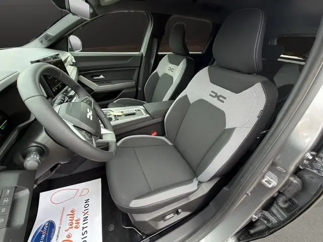 Vue intérieure côté conducteur du Dacia Bigster gris foncé, sièges bi-matière avec logo XC brodé sur appuie-tête.
