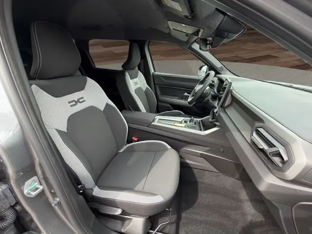 Vue intérieure côté conducteur du Dacia Bigster gris foncé 2026, sièges bi-ton gris clair et foncé avec logo DC brodé.