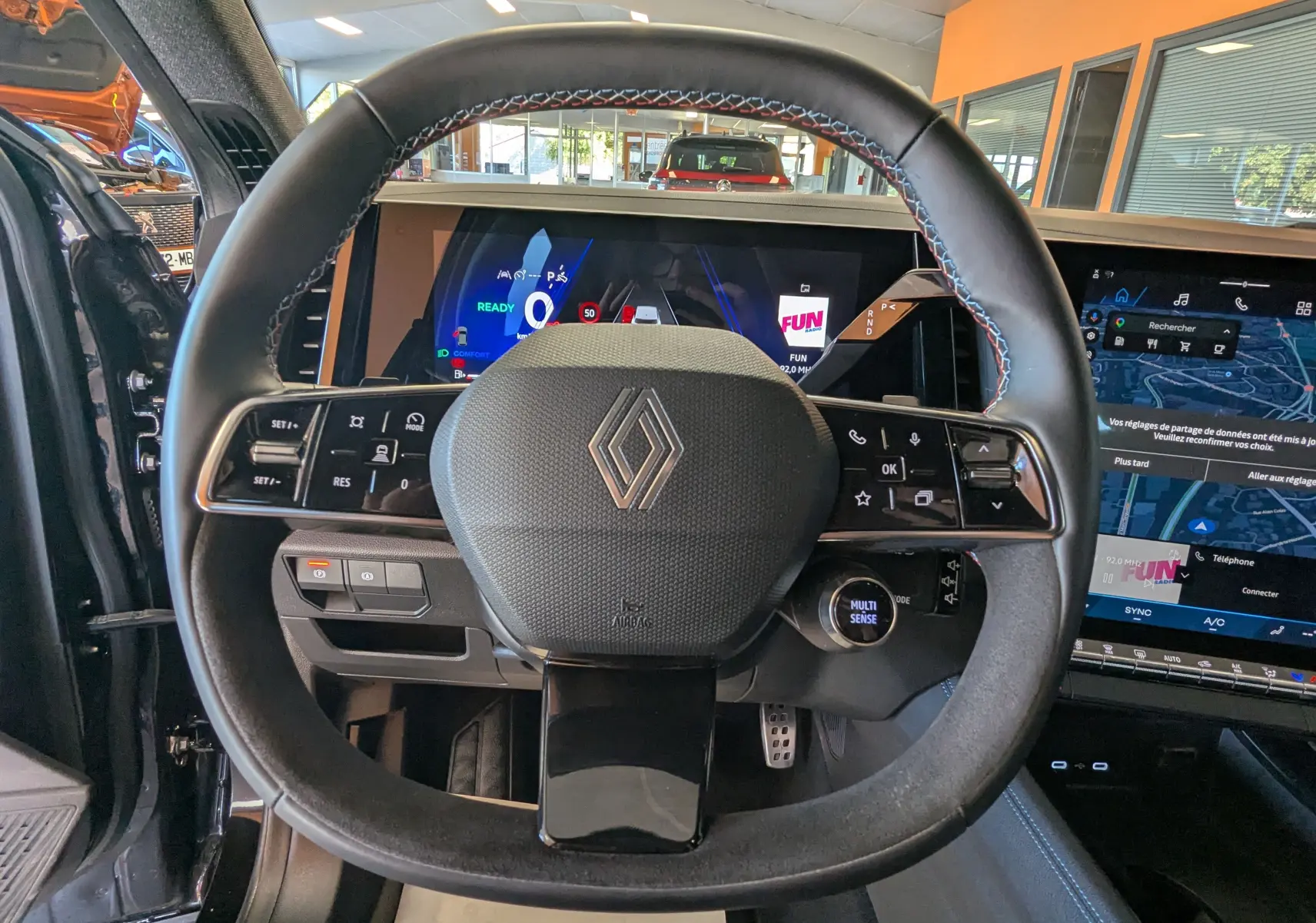 Vue rapprochée du volant noir avec surpiqûres bleues du Renault Espace VI E-Tech, affichages numériques et écran tactile visibles.