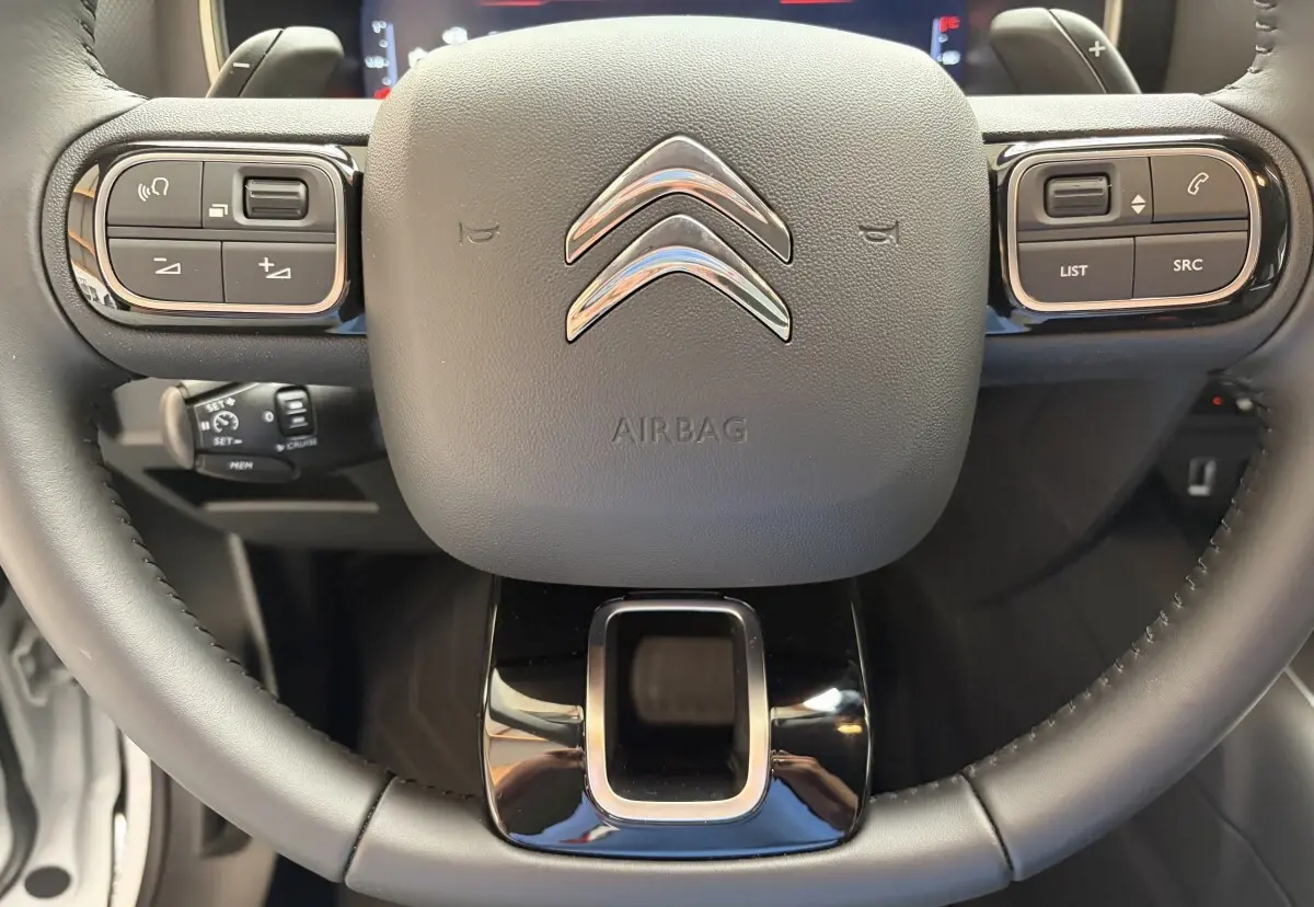 Gros plan sur le volant noir du Citroën C5 Aircross 2025 avec commandes multifonctions et logo chromé central.