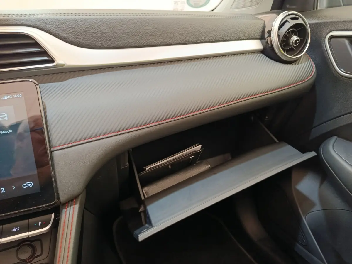 Vue rapprochée de la boîte à gants ouverte côté passager du tableau de bord noir avec surpiqûres rouges du MG ZS Luxury 2024.