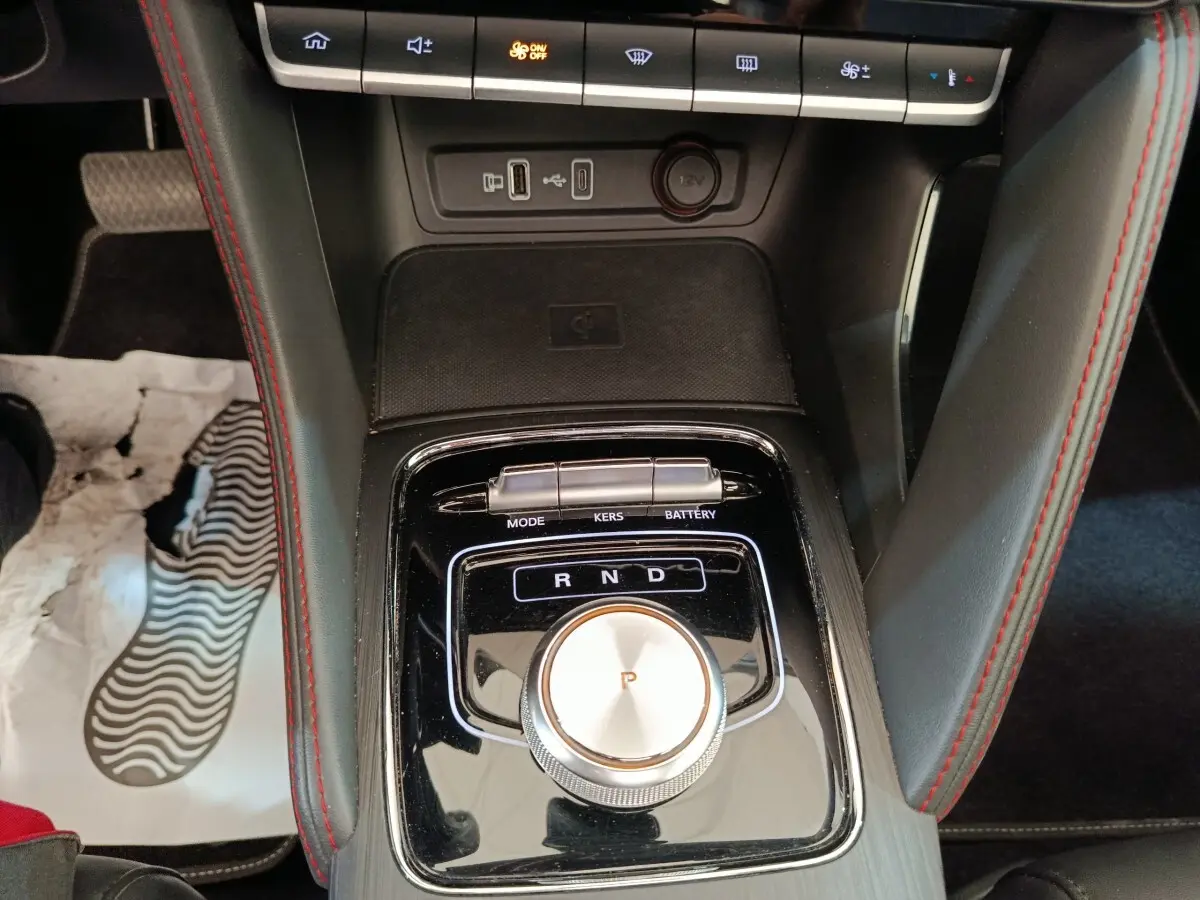 Gros plan sur la console centrale noire du MG ZS Luxury 2024, avec molette de boîte auto et surpiqûres rouges.