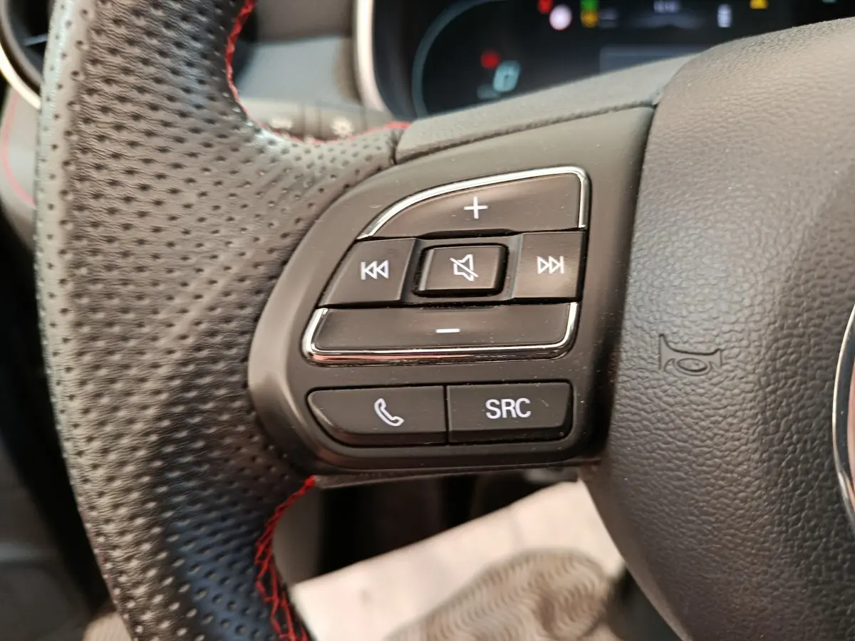 Gros plan sur les commandes gauche du volant noir perforé du MG MOTOR ZS Luxury 2024 avec boutons audio et téléphone.