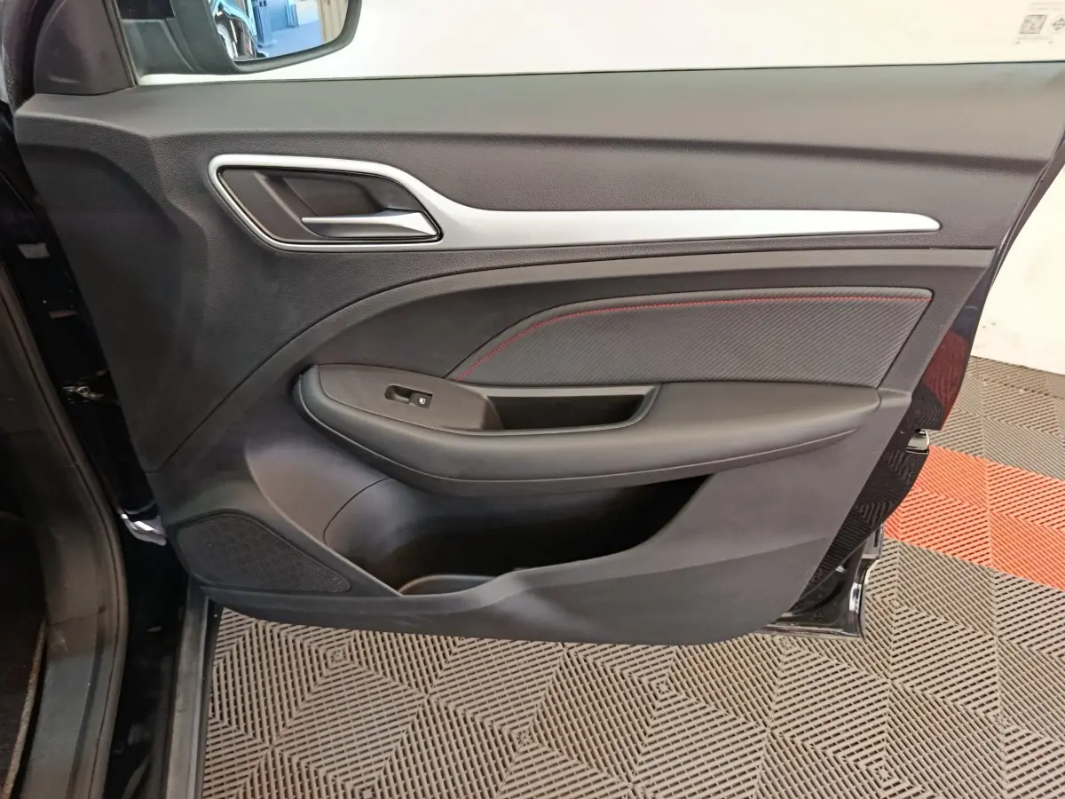 Gros plan sur la porte avant gauche noire du MG ZS Luxury 70kWh 2024, avec poignée et habillage intérieur noir et surpiqûres rouges.