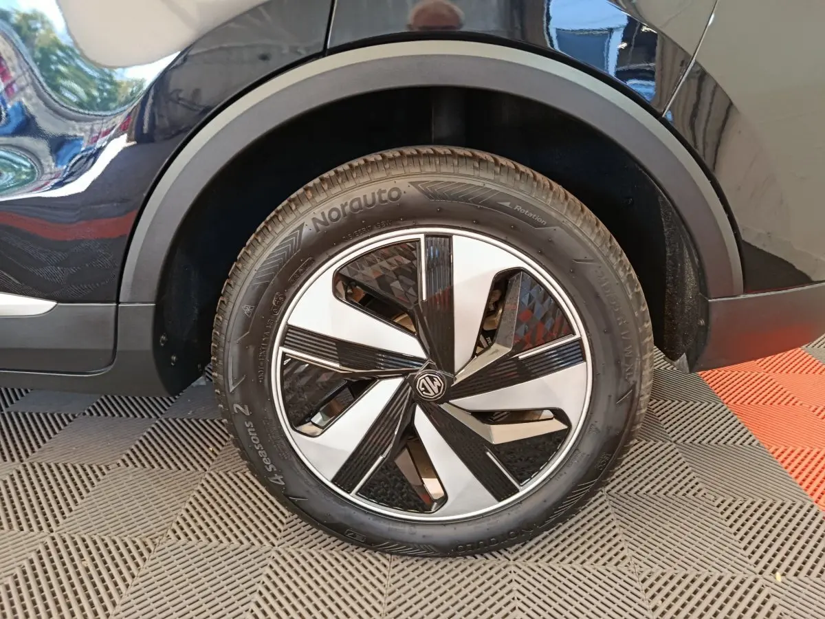 Gros plan sur la roue avant droite noire du MG ZS Luxury 2024 avec jante bicolore et logo MG au centre.